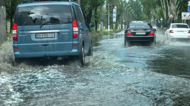 Odessa, Ukrayna -9 Ağustos 2019: sağanak yağışların neden olduğu sel felaketi sırasında su lar altında kalan yolda araba sürmek. Arabalar su üzerinde yüzüyor, sokakları su basayor. Arabaya sıçrat. Büyük bir su birikintisi ile sular altında şehir yolu