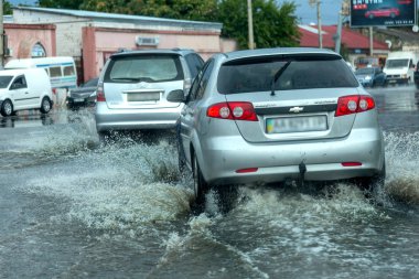 Odessa, Ukrayna - 9 Ağustos 2019: sağanak yağışların neden olduğu sel felaketi sırasında su lar altında kalan yolda araba sürmek. Arabalar su üzerinde yüzüyor, sokakları su basayor. Arabaya sıçrat. Büyük bir su birikintisi ile sular altında şehir yolu