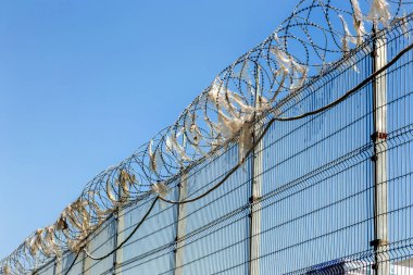 Dikenli tel çit, enkaz yapışan. Mavi gökyüzüne karşı bir deponun koruyucu çit duvarıdikenli dikenli tel çivi üzerinde Yırtık eski plastik torbalar