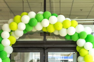 Çok renkli balonlar mağaza salonunun girişini süslüyor. Şenlikli bir arka plan olarak kurumsal sarı, yeşil ve beyaz renklerde şişme renk topları kavramsal tasarım