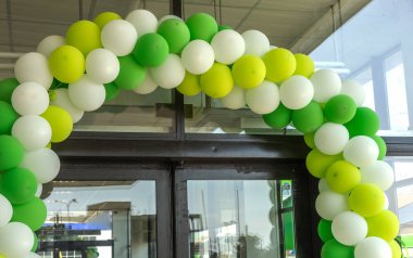 Çok renkli balonlar mağaza salonunun girişini süslüyor. Şenlikli bir arka plan olarak kurumsal sarı, yeşil ve beyaz renklerde şişme renk topları kavramsal tasarım