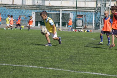 Odessa, Ukrayna - 7 Eylül 2019: Antrenmanda küçük çocuklar futbol oynuyor. Genç çocuklar oyun alanında futbol uyguluyorlar. Çocuklar yeşil futsal sahada futbol oynuyor