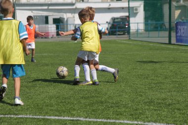 Odessa, Ukrayna - 7 Eylül 2019: Antrenmanda küçük çocuklar futbol oynuyor. Genç çocuklar oyun alanında futbol uyguluyorlar. Çocuklar yeşil futsal sahada futbol oynuyor