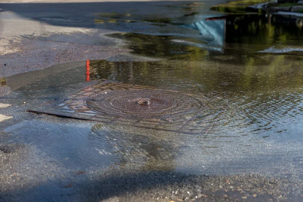 Accident of water supply, sewerage. Water flows from hatch of road sewage system. Dirty sewer flows down fountain along road. Water flows from hatch. Fountain flows down road from sewer — Stock Image Accident Water Supply Sewerage Water Flows Hatch Road Sewage System Stock Photo