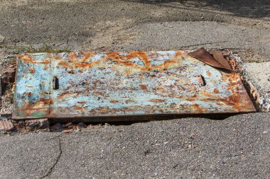 Paslı arka plan. Eski paslı bir metal parçası yolda yatıyor ve eski çatlak asfaltta büyük bir deliği kapatıyor. Kötü asfalt yol