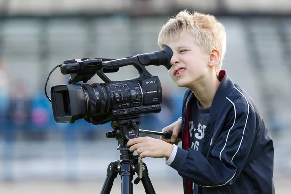 Odessa, Ukrayna - 2019 dolaylarında: Küçük bir çocuk, bir genç, stadyumun yeşil sahasında profesyonel bir video kamera ile 4K video çekiyor. Televizyon kamerası olan genç bir kameraman.