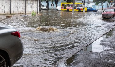 Odessa, Ukraine - May 28, 2020: driving car on flooded road during flood caused by torrential rains. Cars float on water, flooding streets. Splash on car. Flooded city road with large puddle clipart