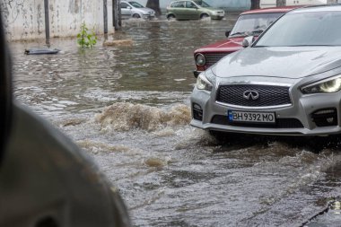 Odessa, Ukrayna - 28 Mayıs 2020: sel baskınları sırasında sel basmış yolda araba kullanmak. Arabalar suda yüzer, sokakları su basar. Arabanın üzerine su sıçradı. Büyük su birikintileriyle dolu şehir yolu.