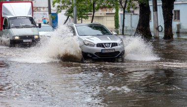 Odessa, Ukrayna - 28 Mayıs 2020: sel baskınları sırasında sel basmış yolda araba kullanmak. Arabalar suda yüzer, sokakları su basar. Arabanın üzerine su sıçradı. Büyük su birikintileriyle dolu şehir yolu.