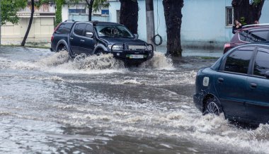 Odessa, Ukrayna - 28 Mayıs 2020: sel baskınları sırasında sel basmış yolda araba kullanmak. Arabalar suda yüzer, sokakları su basar. Arabanın üzerine su sıçradı. Büyük su birikintileriyle dolu şehir yolu.