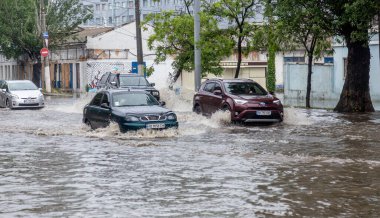 Odessa, Ukrayna - 28 Mayıs 2020: sel baskınları sırasında sel basmış yolda araba kullanmak. Arabalar suda yüzer, sokakları su basar. Arabanın üzerine su sıçradı. Büyük su birikintileriyle dolu şehir yolu.