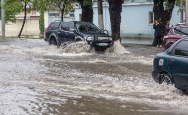 Odessa, Ukrayna - 28 Mayıs 2020: sel baskınları sırasında sel basmış yolda araba kullanmak. Arabalar suda yüzer, sokakları su basar. Arabanın üzerine su sıçradı. Büyük su birikintileriyle dolu şehir yolu.