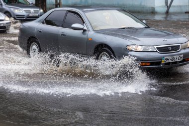 Odessa, Ukrayna - 28 Mayıs 2020: sel baskınları sırasında sel basmış yolda araba kullanmak. Arabalar suda yüzer, sokakları su basar. Arabanın üzerine su sıçradı. Büyük su birikintileriyle dolu şehir yolu.