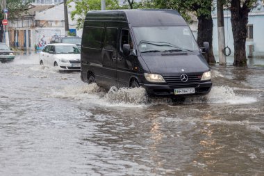 Odessa, Ukrayna - 28 Mayıs 2020: sel baskınları sırasında sel basmış yolda araba kullanmak. Arabalar suda yüzer, sokakları su basar. Arabanın üzerine su sıçradı. Büyük su birikintileriyle dolu şehir yolu.