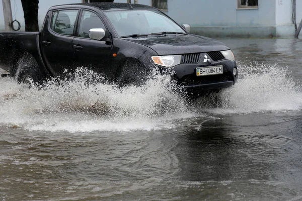 Odessa, Ukrayna - 28 Mayıs 2020: sel baskınları sırasında sel basmış yolda araba kullanmak. Arabalar suda yüzer, sokakları su basar. Arabanın üzerine su sıçradı. Büyük su birikintileriyle dolu şehir yolu.