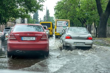 Odessa, Ukrayna - 28 Mayıs 2020: sel baskınları sırasında sel basmış yolda araba kullanmak. Arabalar suda yüzer, sokakları su basar. Arabanın üzerine su sıçradı. Büyük su birikintileriyle dolu şehir yolu.