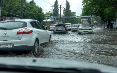 Odessa, Ukrayna - 28 Mayıs 2020: sel baskınları sırasında sel basmış yolda araba kullanmak. Arabalar suda yüzer, sokakları su basar. Arabanın üzerine su sıçradı. Büyük su birikintileriyle dolu şehir yolu.