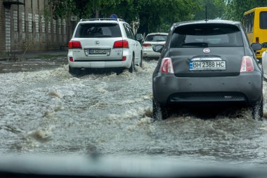 Odessa, Ukrayna - 28 Mayıs 2020: sel baskınları sırasında sel basmış yolda araba kullanmak. Arabalar suda yüzer, sokakları su basar. Arabanın üzerine su sıçradı. Büyük su birikintileriyle dolu şehir yolu.
