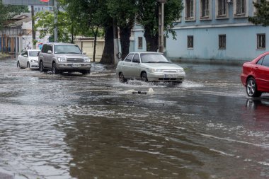 Odessa, Ukrayna - 28 Mayıs 2020: sel baskınları sırasında sel basmış yolda araba kullanmak. Arabalar suda yüzer, sokakları su basar. Arabanın üzerine su sıçradı. Büyük su birikintileriyle dolu şehir yolu.