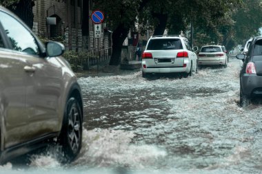 Şiddetli yağmurların yol açtığı sel baskını sırasında sel basmış yolda bir araba. Arabalar suda yüzer, sokakları su basar. Arabanın üzerine su sıçradı. Büyük su birikintileriyle dolu şehir yolu. Şehirde sağanak yağış ardından sel