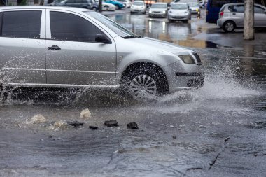 Şiddetli yağmurların yol açtığı sel baskını sırasında sel basmış yolda bir araba. Arabalar suda yüzer, sokakları su basar. Arabanın üzerine su sıçradı. Büyük su birikintileriyle dolu şehir yolu. Şehirde sağanak yağış ardından sel