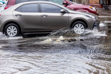 Şiddetli yağmurların yol açtığı sel baskını sırasında sel basmış yolda bir araba. Arabalar suda yüzer, sokakları su basar. Arabanın üzerine su sıçradı. Büyük su birikintileriyle dolu şehir yolu. Şehirde sağanak yağış ardından sel