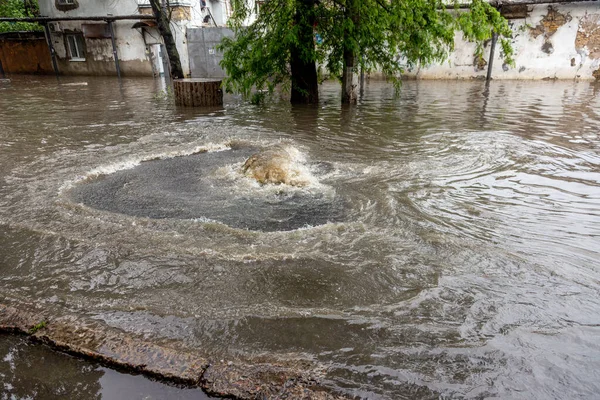 都市の大雨の後に洪水 下水は開いているアスファルトを破壊し 噴水を爆破した 汚れた下水は嵐の下水道を突破し 雨の後に街の通りにこぼれた 流行や感染の危険性 — ストック写真