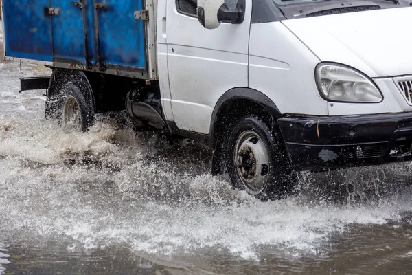 riving car on flooded road during flood caused by torrential rains. Cars float on water, flooding streets. Splash on car. Flooded city road with large puddle. Flooding after heavy rains at city