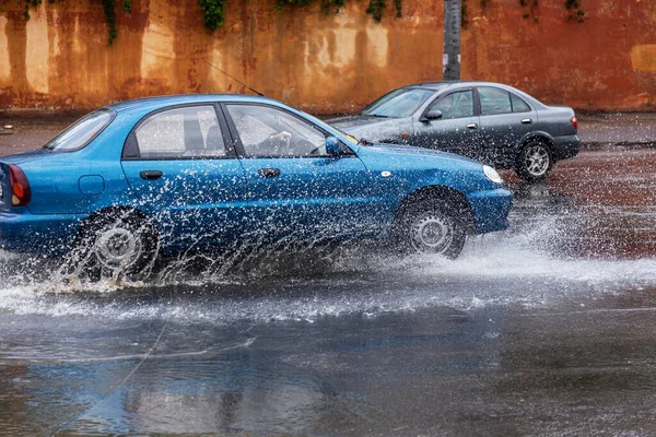 riving car on flooded road during flood caused by torrential rains. Cars float on water, flooding streets. Splash on car. Flooded city road with large puddle. Flooding after heavy rains at city