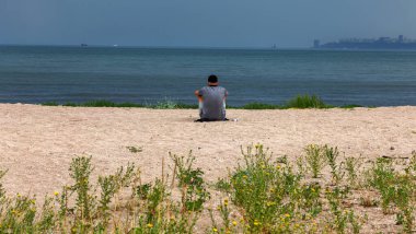 Delikanlı, sakin ol. Deniz kıyısındaki iskelede otururken gün batımından dosdoğru sana bakıyor. Yazın arka planda bir şeye odaklanmak ve düşünmek için kavramsal alan etiketli metin pankartı