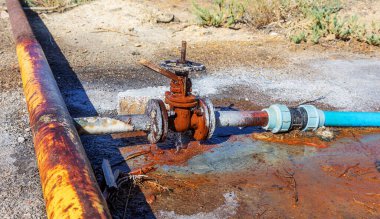 Eski su vanası. Akan su birikintisinde paslı bir su vanası. Açık hava tesisatında geniş ve paslı sızıntı vanası. Paslı, bozuk tesisat.