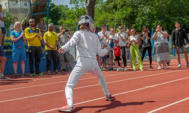 Odessa, Ukrayna - 9 Haziran 2020: Bir spor etkinliği sırasında yapılan gösteri sırasında stadyum yolunda maske ve beyaz eskrim kostümü giyen genç bayan sporcu. Pistte eskrim