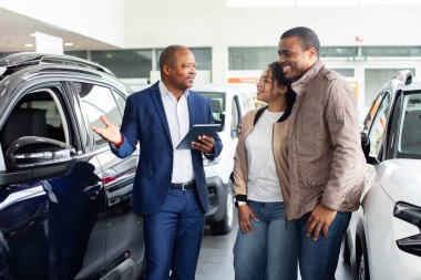 Happy black couple with dealer in showroom, cheerful discussion about SUV purchase, lifestyle concept of transport, modern business and finance auto shopping experience.