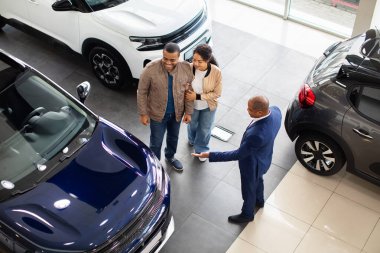Top view of African American couple with dealer in showroom discussing new SUV, lifestyle and business moment of auto shopping, consultation, finance and purchase