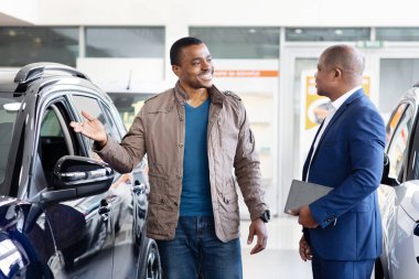 African American customer talking with car dealer in showroom, smiling while discussing new vehicle options, lifestyle and finance moment of auto sales and transport