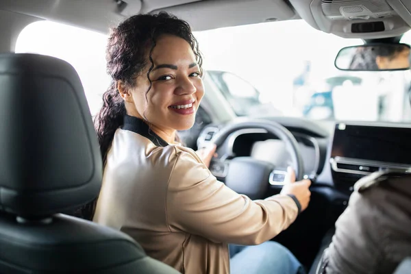 Smiling African American woman sitting in driver seat of new car, lifestyle concept of auto purchase, ownership, transport, finance and customer satisfaction