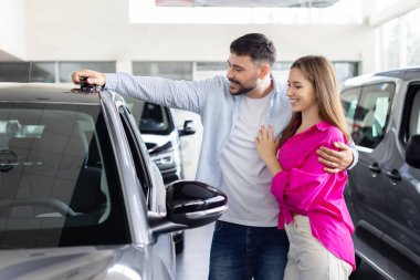 Young caucasian spouses smiling while choosing car in dealership showroom, lifestyle moment of auto shopping, vehicle choice and modern transport purchase decision