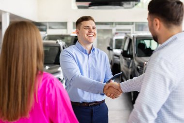 Smiling car dealer shaking hands with customer at showroom, happy couple finalizing vehicle purchase decision. Lifestyle, transportation and trust concept in dealership