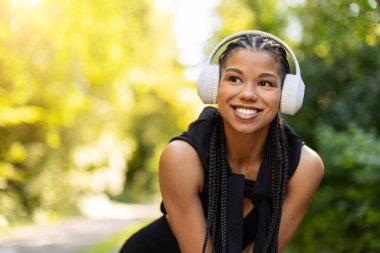 Closeup of smiling African American woman with braided hair and headphones enjoying outdoor jogging break, representing fitness and positive energy