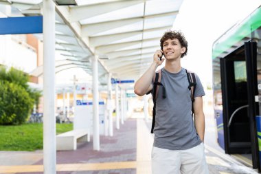 Young Caucasian man smiling while talking on smartphone at airport terminal. Represents communication, connection, modern travel, and youthful lifestyle