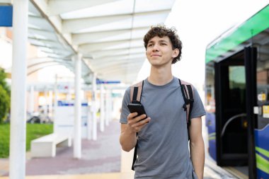 Young Caucasian man with backpack holding smartphone at airport terminal. Concept of travel, waiting, modern lifestyle, and exploring new destinations