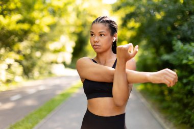 Focused young black woman stretching arms before run in park. Outdoor fitness, warmup routine, strength and motivation for active healthy lifestyle