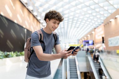 Young Caucasian man with backpack looking at passport and boarding pass along with smartphone. Modern travel lifestyle, youth journey, and airport departure routine