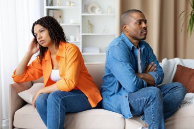 Üzgün Afro-Amerikalı çift evdeki kanepede yan yana oturuyor, ciddi ifadelerle başlarını çeviriyorlar. İlişki sorunları, stres, yaşam tarzı ve aile içi çatışma kavramı