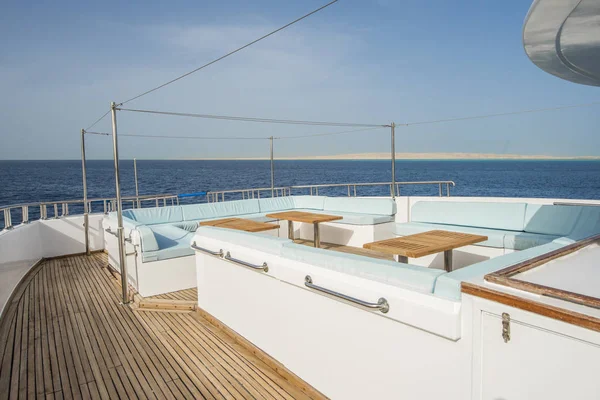 Bow teak deck of a large luxury motor yacht with chairs sofa table and tropical sea view background