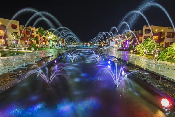 Ornate fountain water feature lit up at night by large swimming pool in a luxury tropical hotel resort