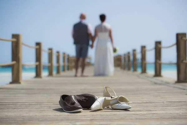 Wedding couple on wooden pier with shoes in foreground — Stock Photo, Image