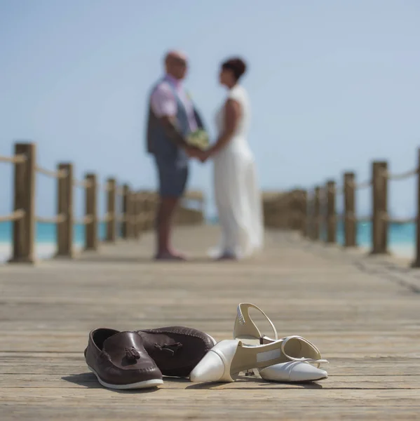 Wedding couple on wooden pier with shoes in foreground — Stock Photo, Image