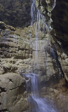 Bir yeraltı mağarasında jeolojik kaya oluşumları ve şelale
