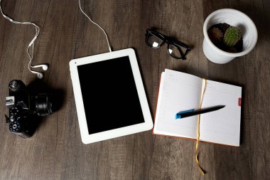 Vintage fotoğraf makinesi, dijital tablet ile kulaklıklar, notlar, gözlük ve kaktüs yalan üzerine kahverengi ahşap bir masa, bir kalem ile günlük görünümü top